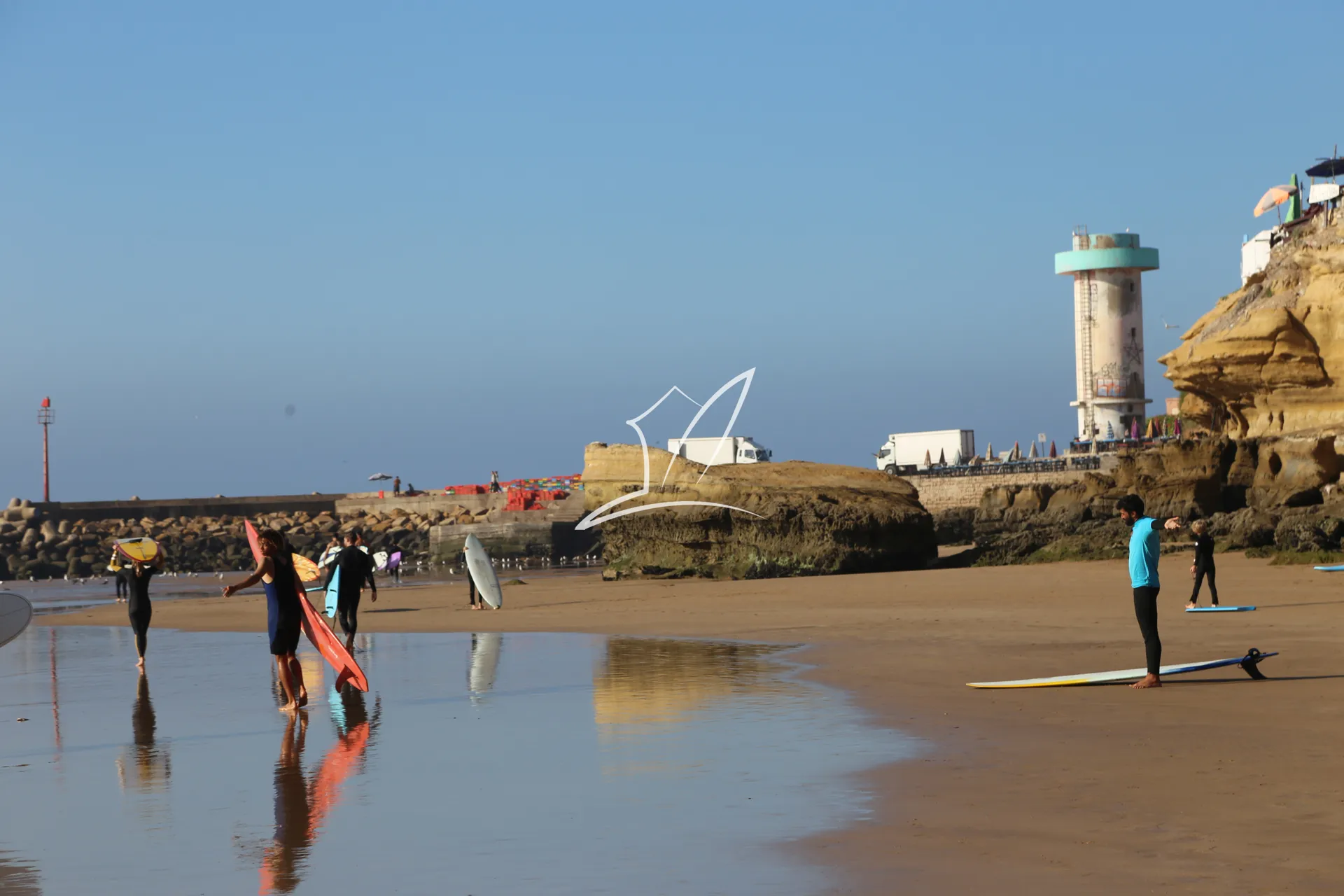 Surfers walking on a wet beach below a lighthouse