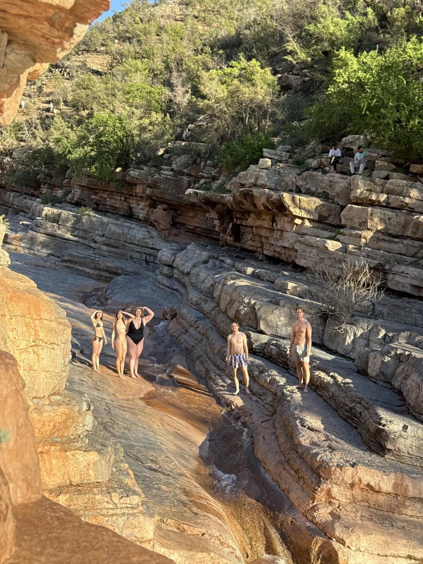 Visitors standing on layered rock beside a natural pool channel in Paradise Valley