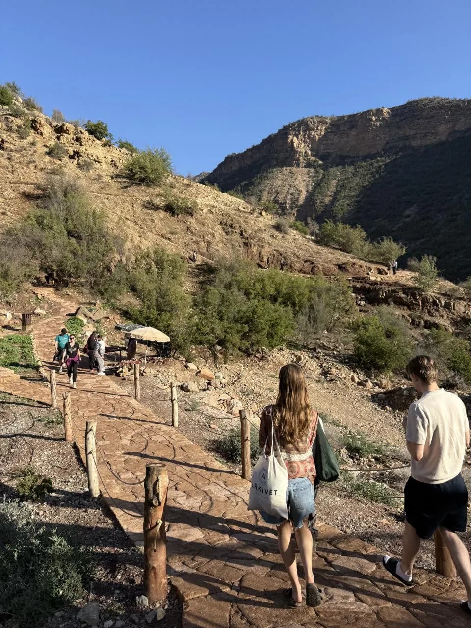 Visitors walking a paved path up a rocky hillside under a blue sky