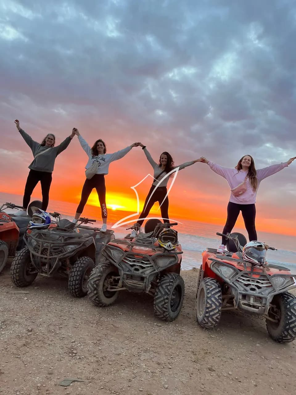 Friends standing on quad bikes under a sunset sky