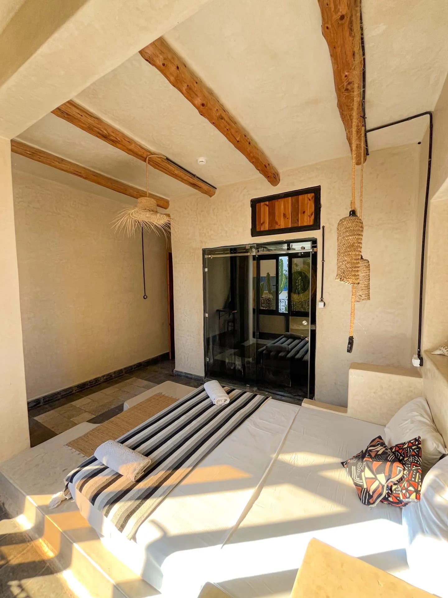Room with wooden ceiling beams, a striped bed and a glass shower door